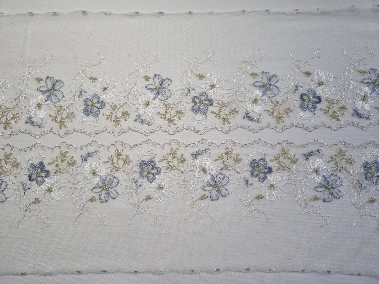 Wit tule kant met wit en lichtblauw geborduurde bloemen