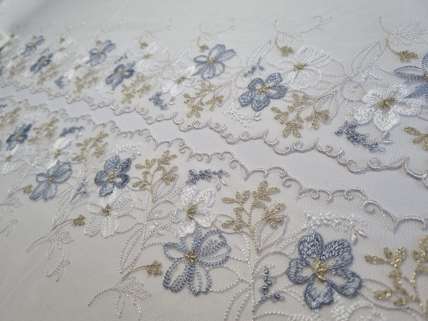 Wit tule kant met wit en lichtblauw geborduurde bloemen