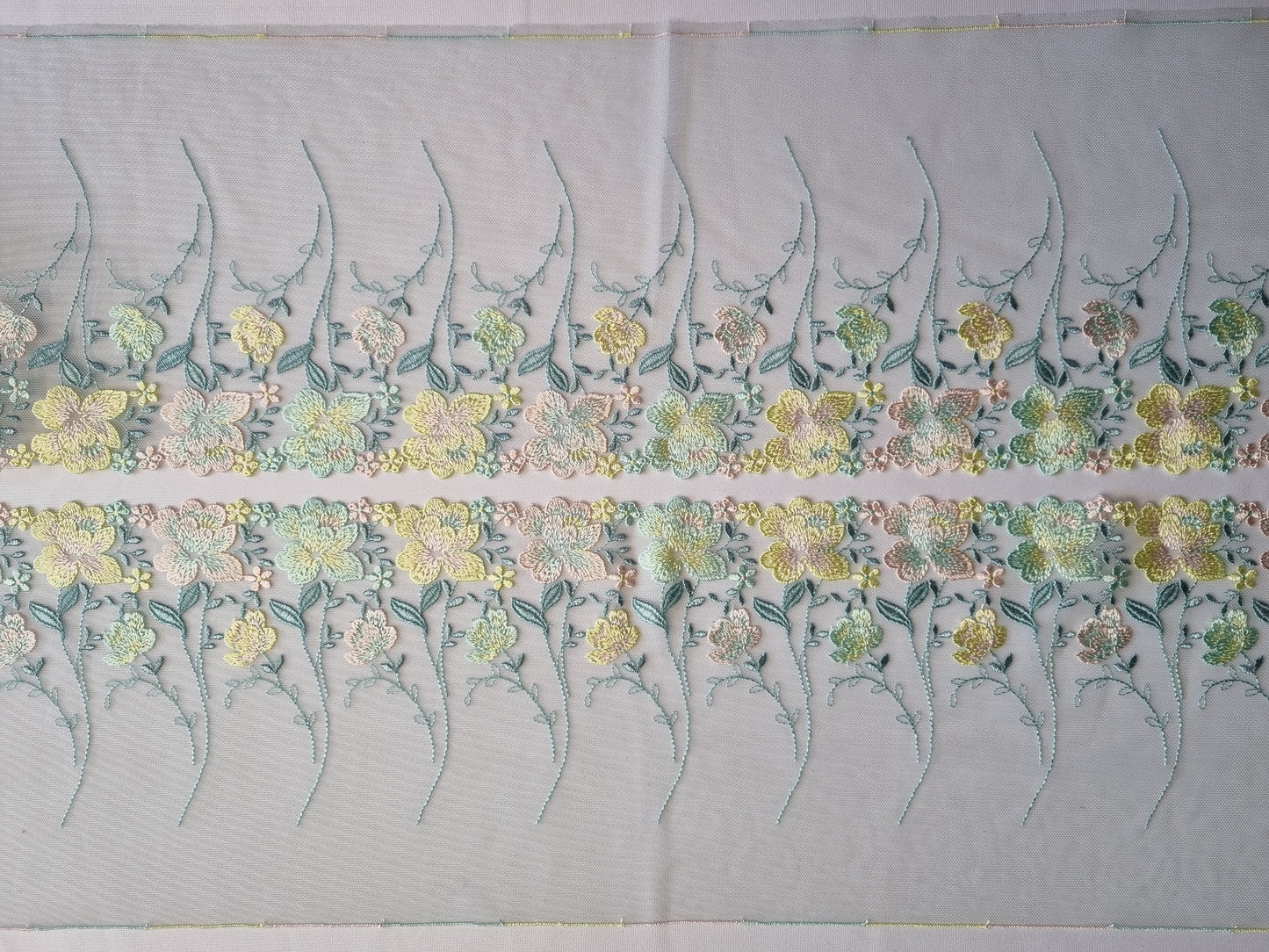 Mint kleurig tule kant met licht roze, mint en zacht geel geborduurde roosjes