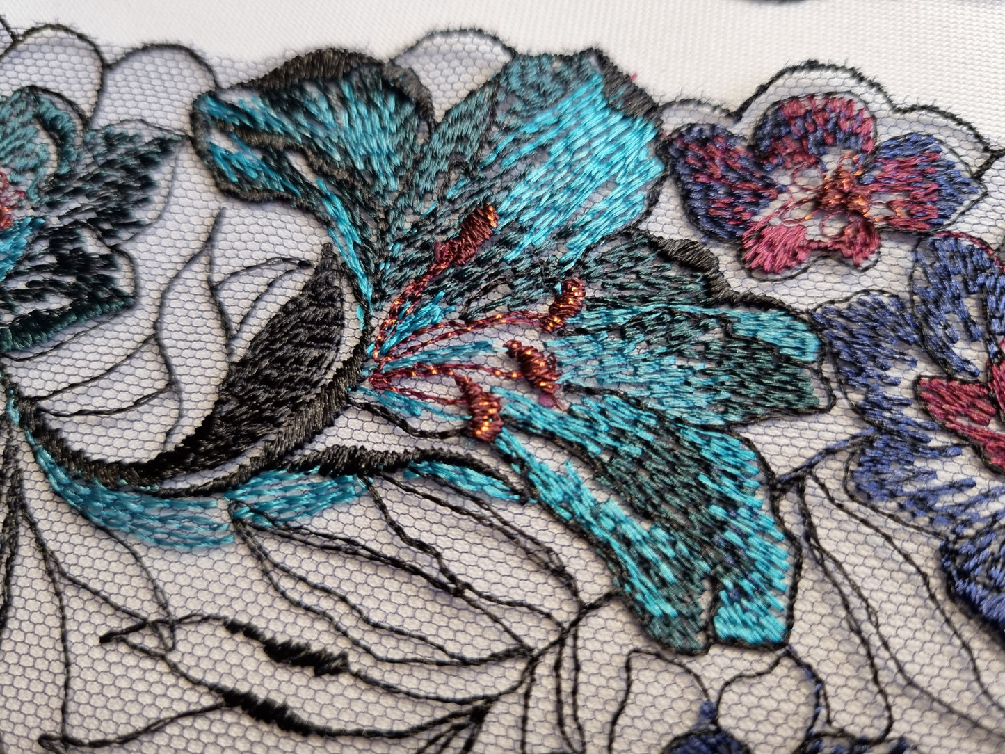 Zwart tule kant met geborduurde lelies in aubergine en turquoise