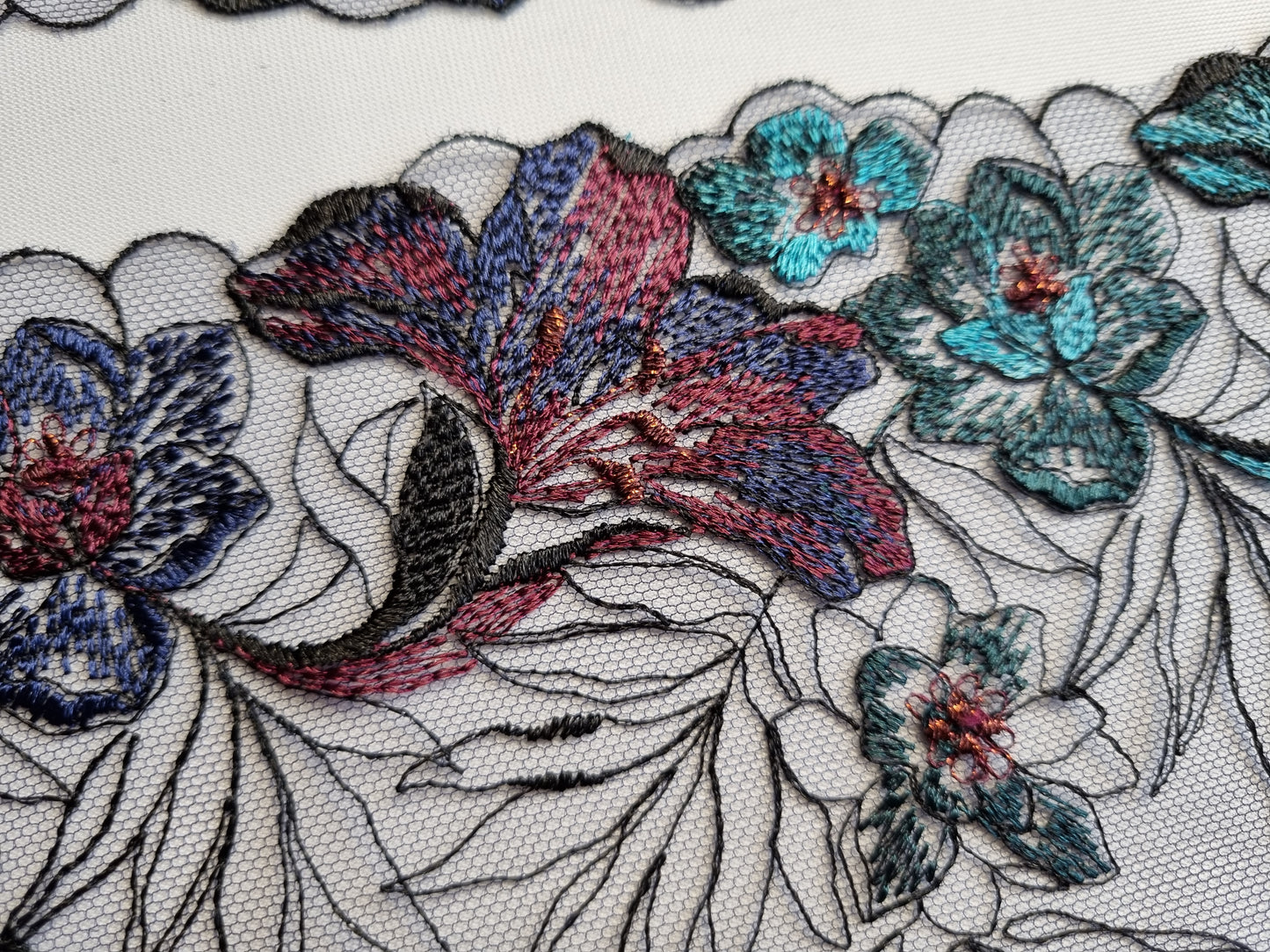 Zwart tule kant met geborduurde lelies in aubergine en turquoise