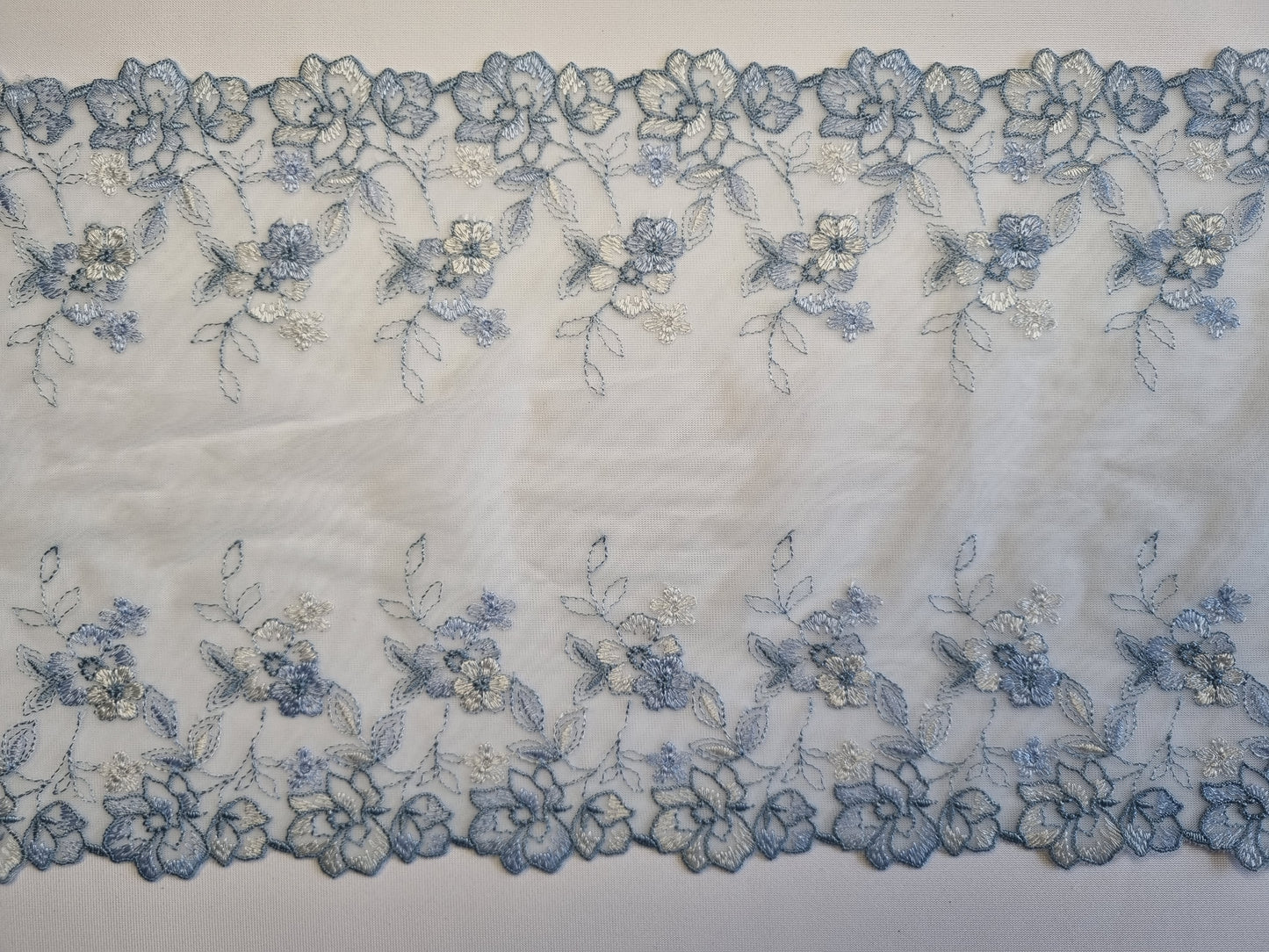 Lichtblauw tule kant met geborduurde bloemen in blauwtinten