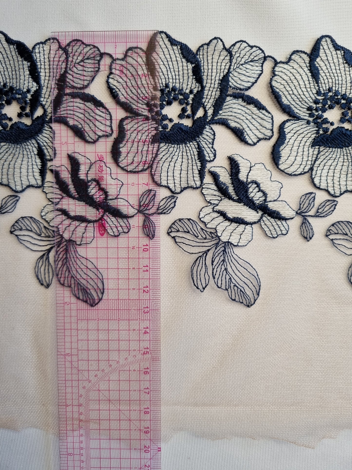 Beige kleurig tule kant met grote donkerblauw met wit geborduurde bloemen.