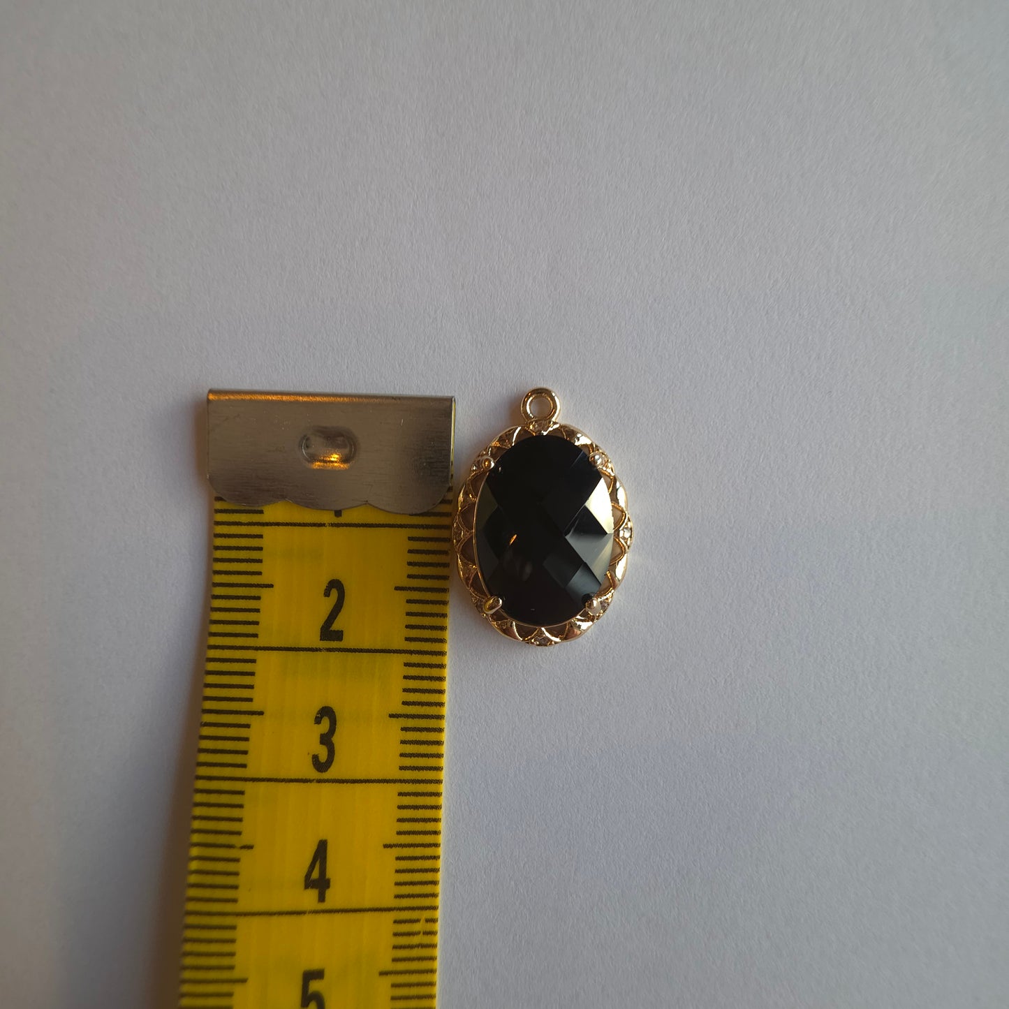 goud kleurig bedeltje met zwart zirkoon voorzien van rand die ingezet is met witte zirkoontjes