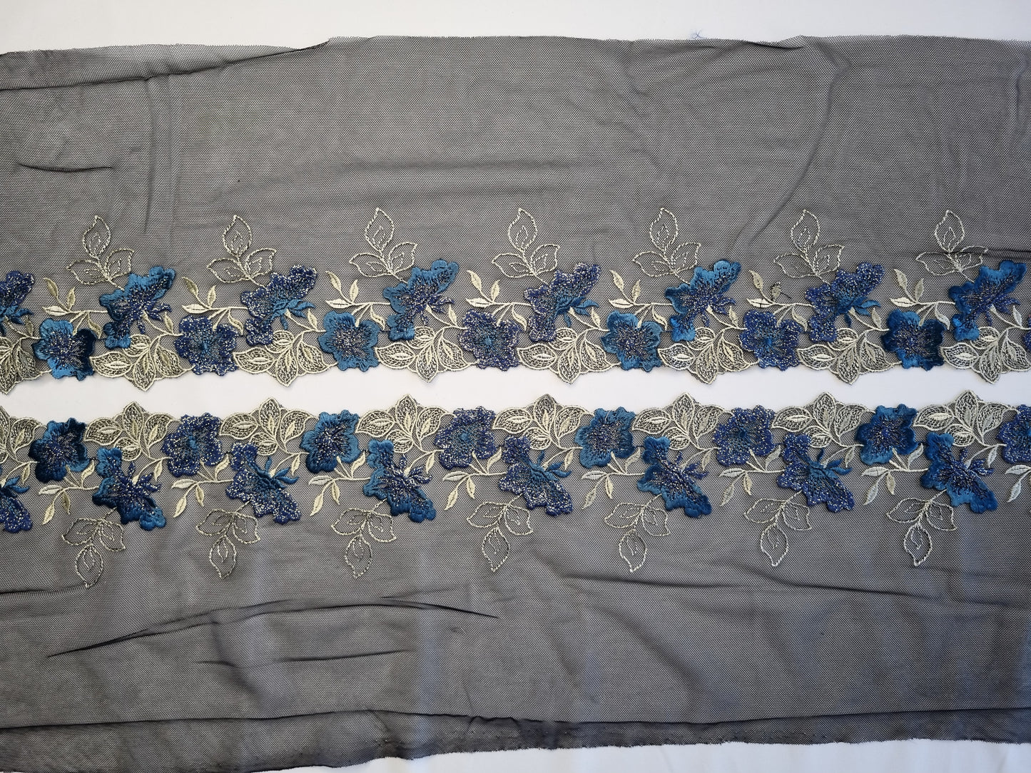 Zwart tule kant met blauwe geborduurde bloemen en goudkleurige lurex draad.