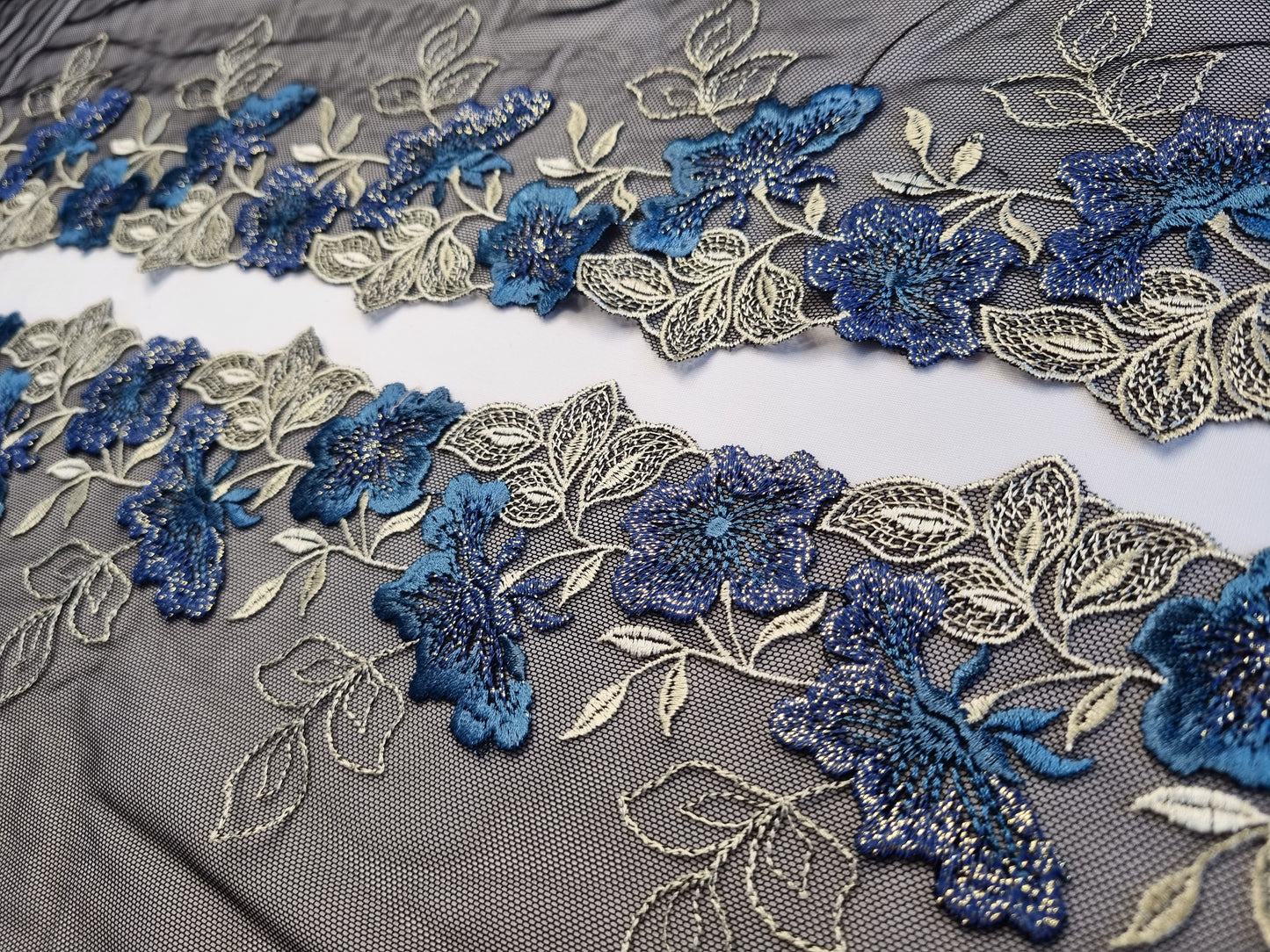 Zwart tule kant met blauwe geborduurde bloemen en goudkleurige lurex draad.
