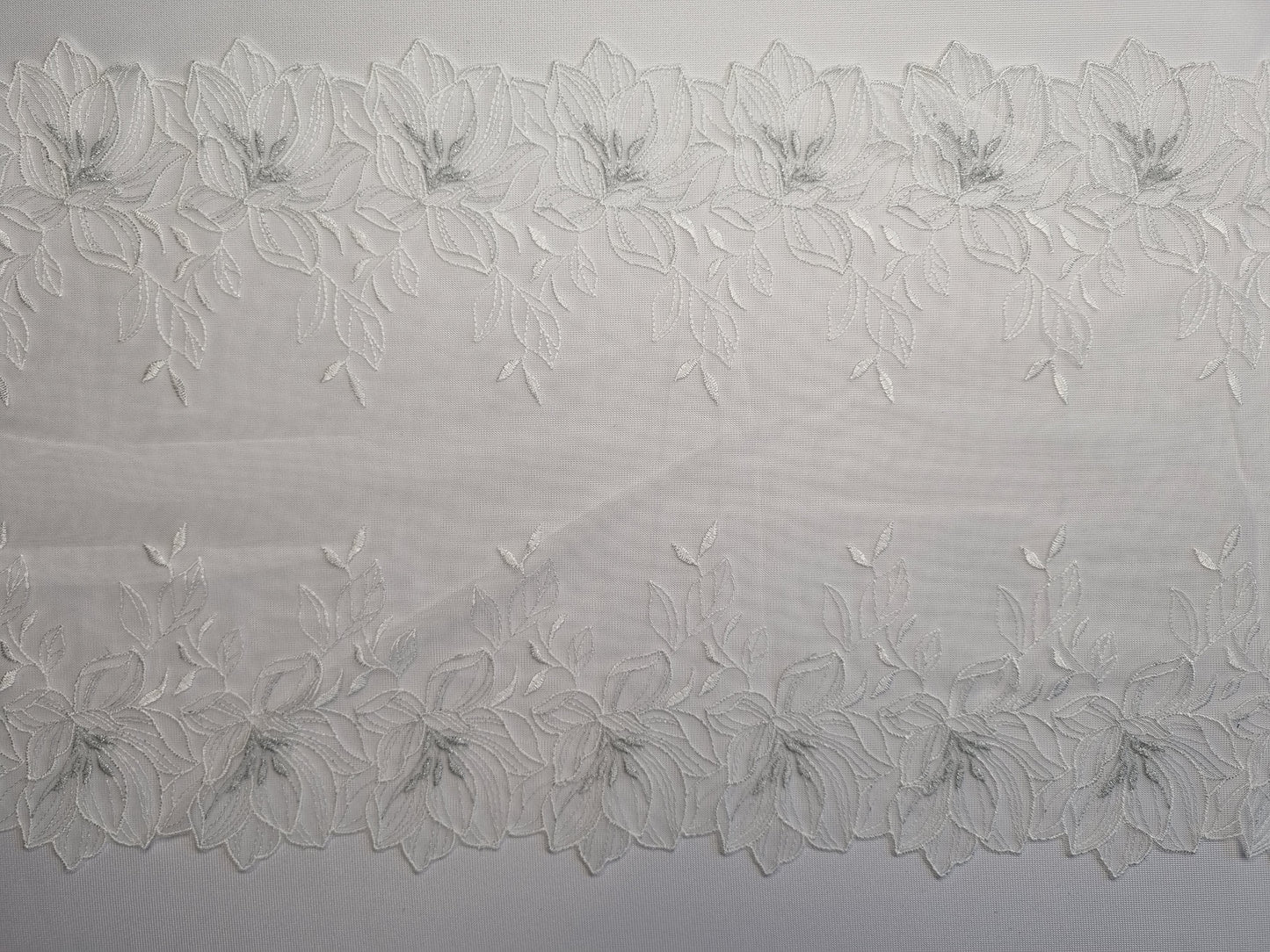 Wit tule kant met wit geborduurde lelies en zilverkleurig hartje van lurex draad